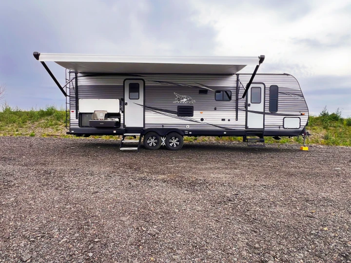 Experience freedom with this RV rental! A grey travel trailer, awning out, and outdoor kitchen ready on a gravel lot.. Jayco Jayflight 2021