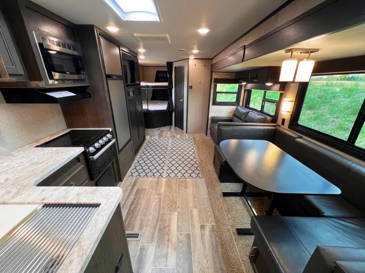 Spacious RV rental interior featuring a full kitchen, dining booth, sofa, and rear bunk beds, ideal for travel.. Jayco Jayflight 2021