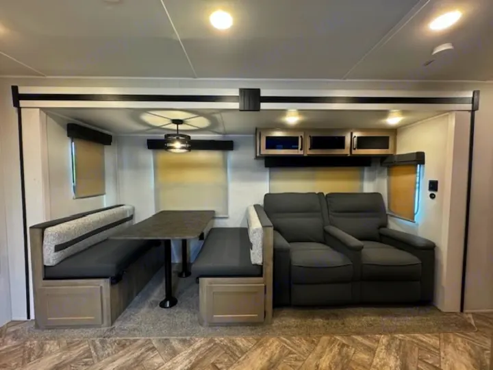 Modern RV rental interior: dinette with table and benches, plus a cozy two-seat reclining sofa. Ideal for comfortable travel.. Palomino Puma 2023