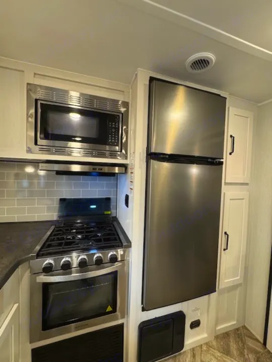 RV rental kitchen showcases stainless appliances: built-in microwave, gas range/oven, large fridge, and light cabinetry with tile.. Palomino Puma 2023