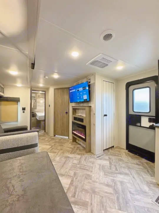RV rental interior: Modern living space with TV, electric fireplace, and bedroom access, ideal for comfortable travel.. Palomino Puma 2023