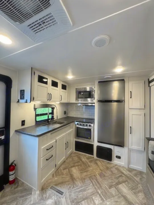 RV rental kitchen: stainless steel appliances, light cabinets, dark counters, and patterned flooring. Ready for travel!. Palomino Puma 2023