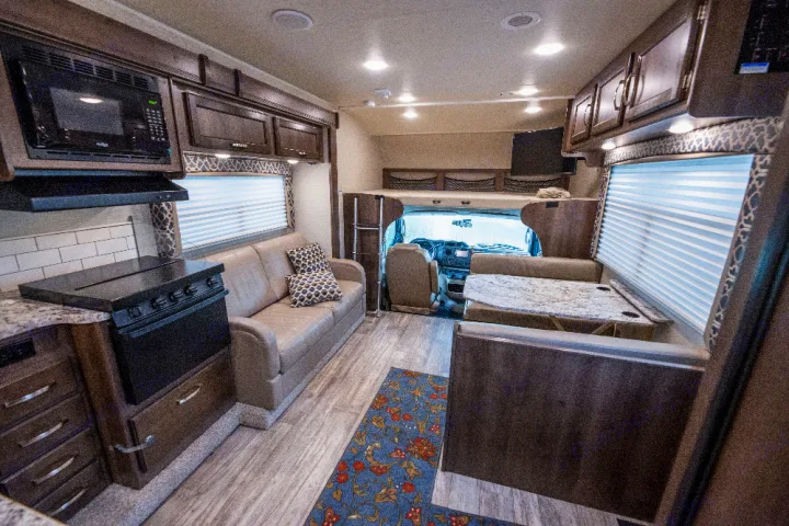 Spacious RV rental interior featuring a kitchen, sofa, dinette with table, and an overhead sleeping bunk.. Jayco Redhawk 2018