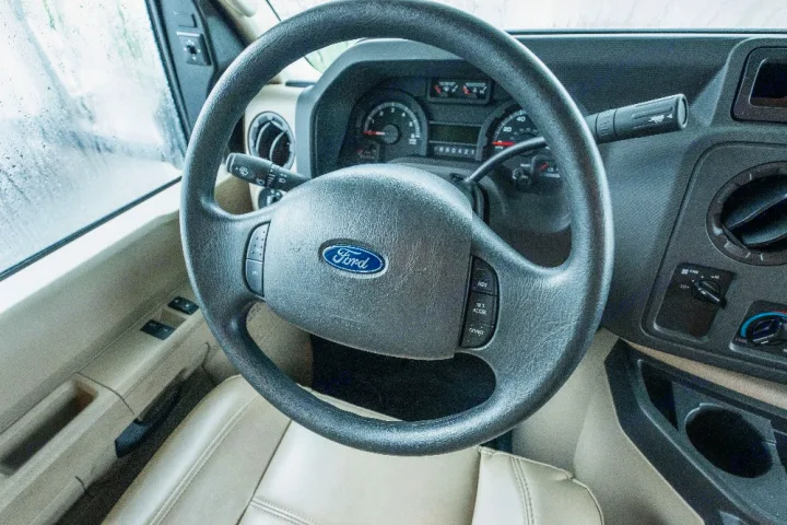 Inside a Ford RV rental: driver's seat, steering wheel, dashboard controls. Rain is visible on the side window.. Jayco Redhawk 2018