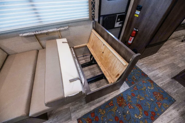 Inside this RV rental, a dinette bench's cushion is lifted, revealing practical under-seat storage.. Jayco Redhawk 2018