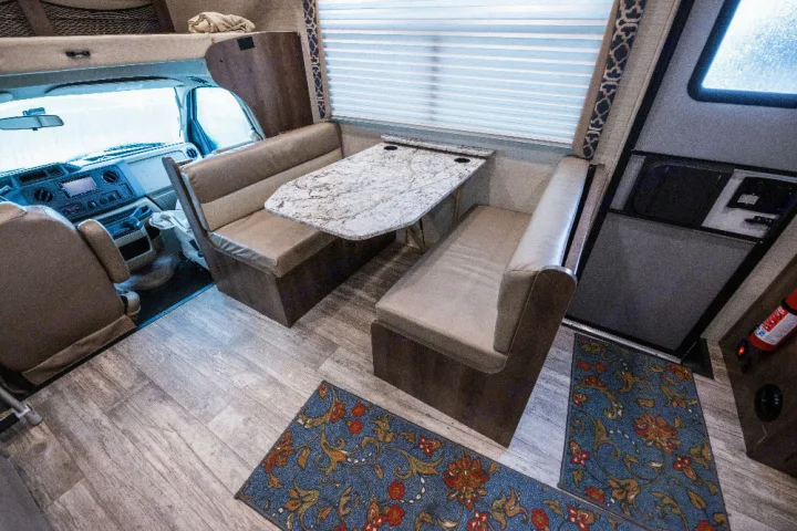 Inside this RV rental: a modern interior with a cozy dining booth, cockpit, and overhead bunk, designed for comfortable travel.. Jayco Redhawk 2018