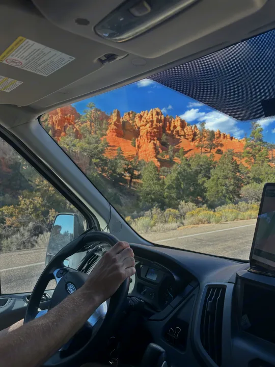 Scenic rv rental drive past stunning red rock formations. Inside, a Ford van's dashboard and driver's hand are visible.. FORD Ford Transit 2015
