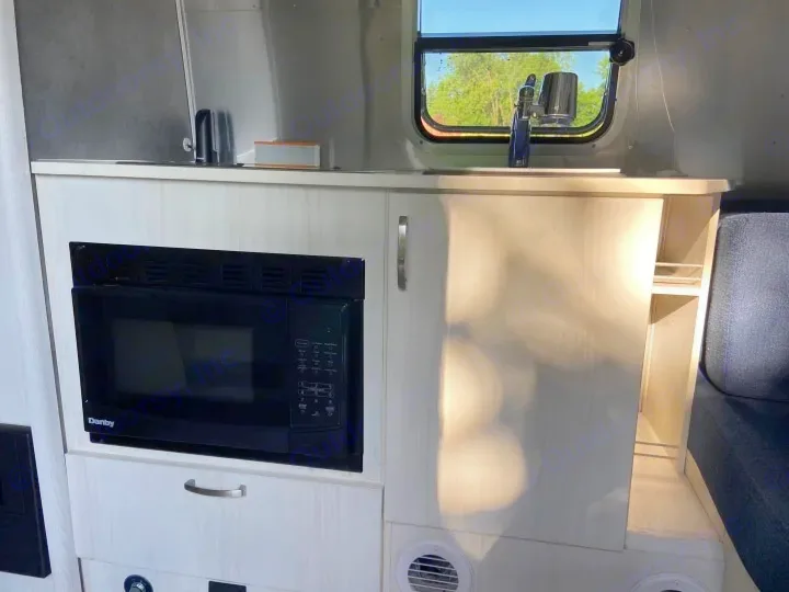 RV rental's light-toned kitchen area with a black Danby microwave, sink, and cabinets, bathed in natural light.. Airstream Airstream 2020