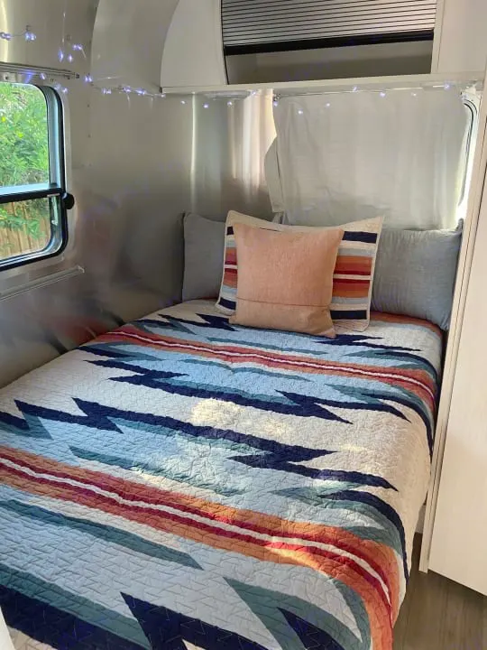 Inside a comfortable rv rental: a bed with a vibrant Southwestern quilt, soft pillows, and twinkling fairy lights.. Airstream Airstream 2020
