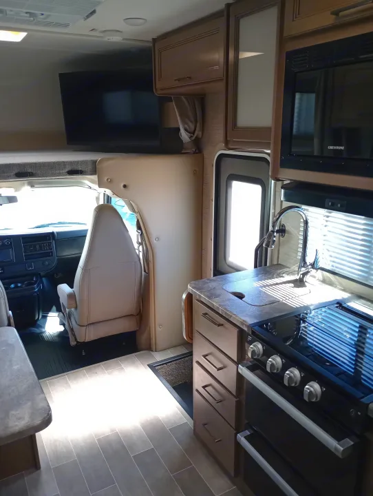 Clean rv rental interior with kitchen (stove, sink, microwave), mounted TV, and front cockpit area.. Thor Chateau 2022