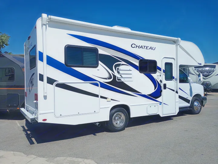This white Chateau RV rental, a Class C motorhome featuring dynamic blue/black graphics, is parked outdoors on asphalt.. Thor Chateau 2022