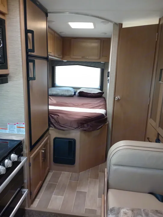 Inside this RV rental: compact kitchen with stove & fridge, a cozy bedroom, and a peek at the dinette seating.. Thor Chateau 2022