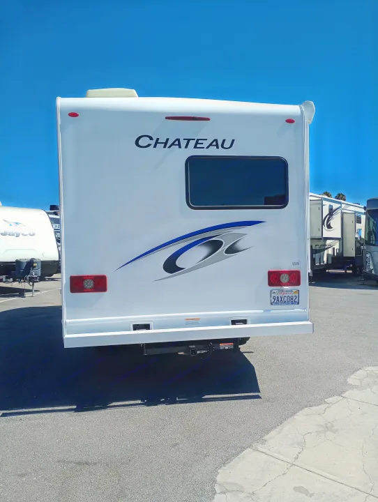 Rear view of a white Chateau RV, ideal for an RV rental adventure, parked outdoors under a clear blue sky.. Thor Chateau 2022