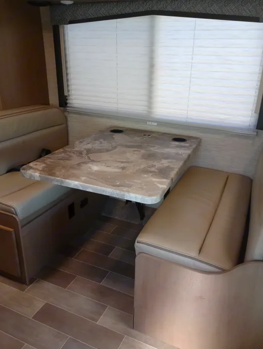 This RV rental features a cozy dinette with beige seating, a marble table, and window blinds, ideal for travel.. Thor Chateau 2022