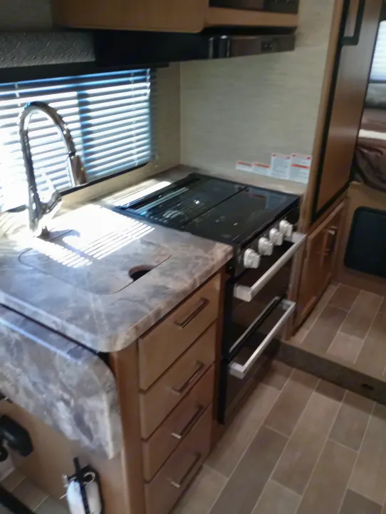 Inside an RV rental: a well-equipped kitchen featuring a sink, stove/oven, and storage drawers. Sunlit interior.. Thor Chateau 2022