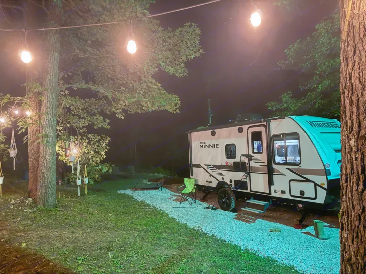 Winnebago Micro Minnie RV rental at a cozy night campsite, illuminated by string lights strung between trees.. Winnebago Minnie Winnie 2022