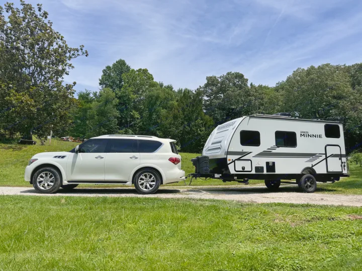 White SUV parked, hitched to a Winnebago Micro Minnie RV rental, on a gravel path surrounded by green trees & grass.. Winnebago Minnie Winnie 2022