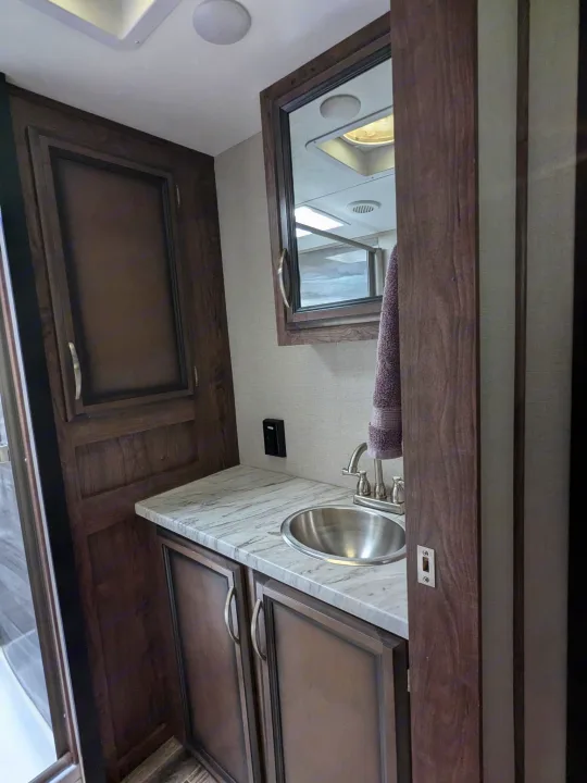 Inside an RV rental: a compact bathroom showing a wooden vanity, stainless steel sink, and dark cabinets.. K-Z Manufacturing Venom V3411TK 2020