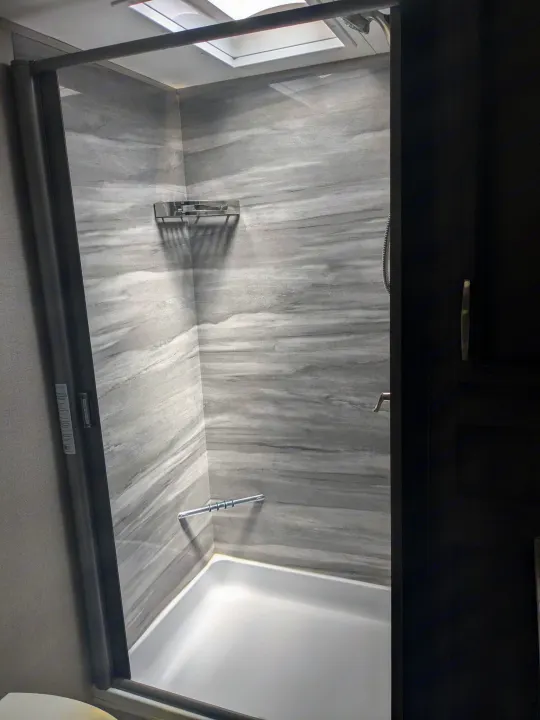 Modern RV rental shower: grey marbled-look walls, white base, skylight, and clear glass door.. K-Z Manufacturing Venom V3411TK 2020