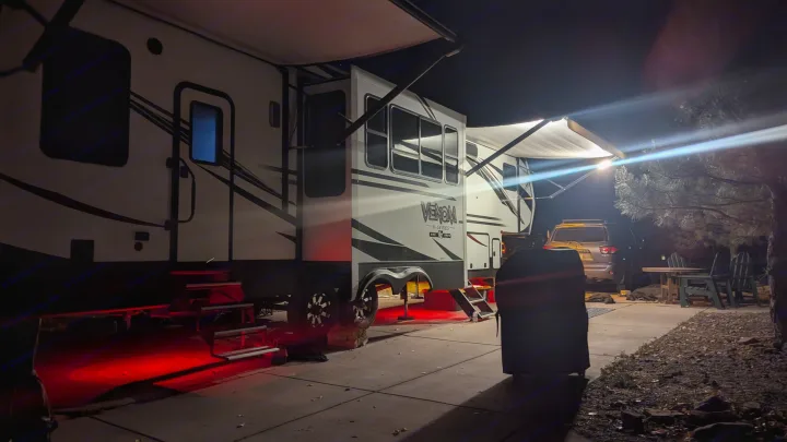 Nighttime RV rental at a campsite. A large white camper with extended awnings, bright lights, and cool red underglow.. K-Z Manufacturing Venom V3411TK 2020