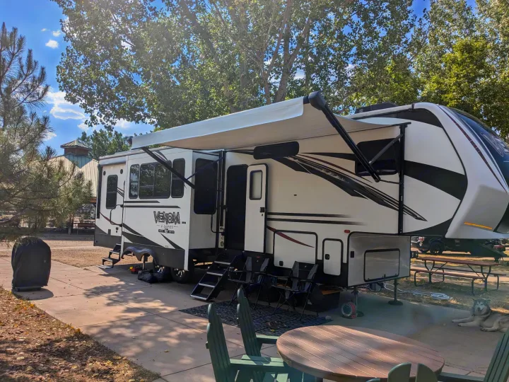 Enjoying the outdoors with this large RV rental setup, featuring an extended awning, patio, and a relaxing dog at a sunny campground.. K-Z Manufacturing Venom V3411TK 2020