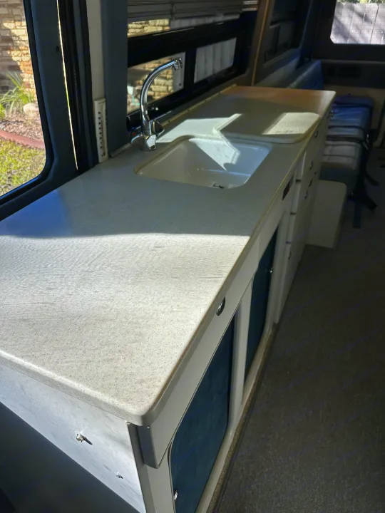 Bright RV rental kitchen: spacious, speckled counter with sink, faucet, and a thermometer next to the window.. Sportsmobile Custom Design 2006