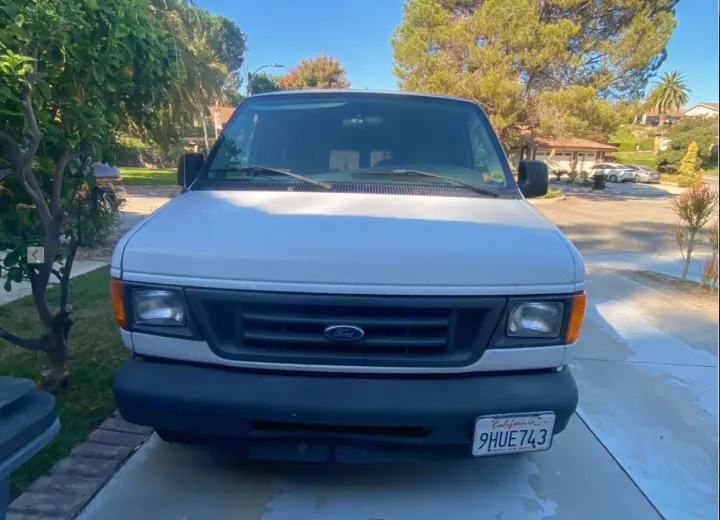 Front view of a white Ford Econoline van (CA plate 9HUE743) parked on a driveway, ideal for an RV rental adventure.. Ford Econoline 150 2003
