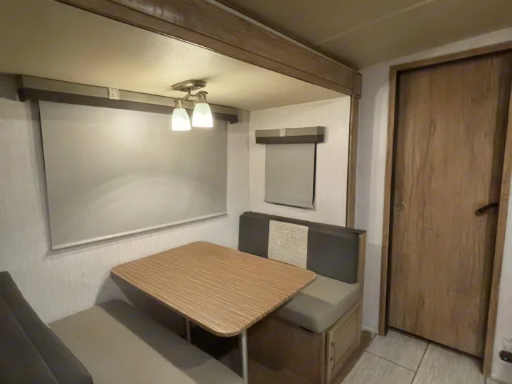 Compact RV rental interior featuring a cozy dinette with bench seating, a window with shade, and a door.. Forest River Palomino Solaire 2021