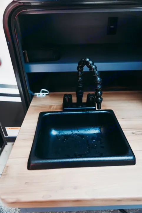 RV rental outdoor kitchen: black sink, flexible faucet, wood counter, and open storage compartment.. Forest River Tracer 2024
