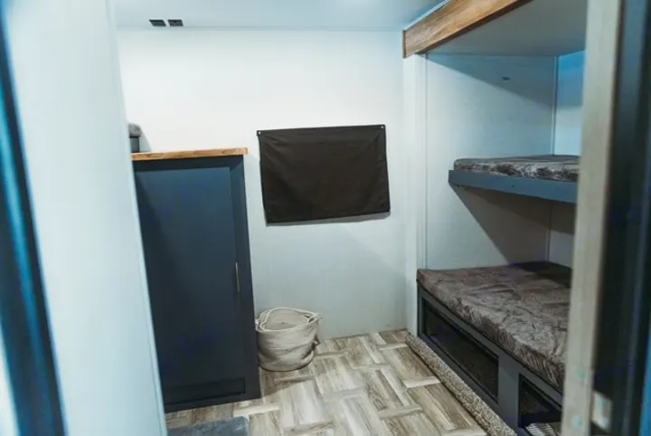 Interior of an RV rental: modern bunk beds with furry mattresses, a dark cabinet, and woven basket storage.. Forest River Tracer 2024