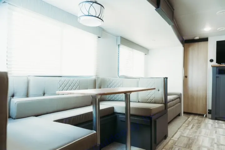 Bright RV rental interior showing a U-shaped dinette with grey booth seating, a wooden table, and large windows with blinds.. Forest River Tracer 2024