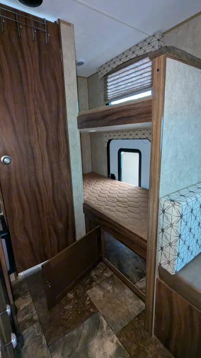Cozy rv rental with stacked bunk beds, showing the lower mattress, a closet, and patterned seating. Compact and inviting.. Coachmen Viking 2017