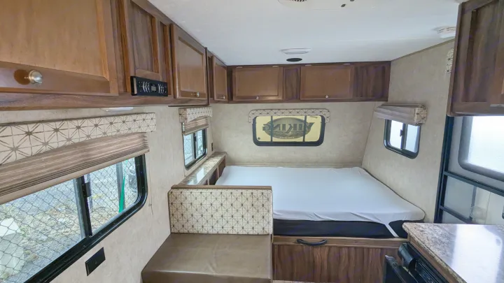 View of a compact RV rental interior with a cozy bed, dinette, overhead cabinets, and windows, ready for adventure.. Coachmen Viking 2017