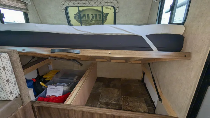 This RV rental's under-bed storage reveals organized camping gear in bins. A bed with white sheets sits above, with windows reflecting a 'Viking' logo.. Coachmen Viking 2017