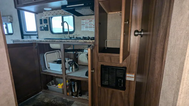 RV rental kitchen interior featuring a sink, stove, open storage cabinet, and a furnace vent. Ready for use.. Coachmen Viking 2017