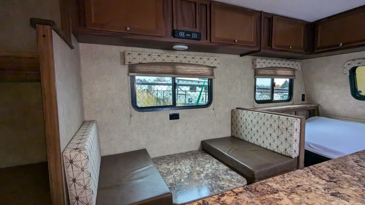 Spacious RV rental interior with a dinette, overhead cabinets, and windows. A comfortable bed is visible in the background.. Coachmen Viking 2017