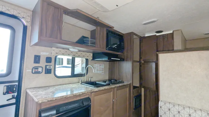 RV rental's compact kitchen. Features dark wood cabinets, granite-look counter, sink, stovetop, and microwave.. Coachmen Viking 2017