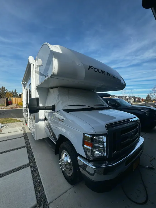 A white Four Winds Class C motorhome with a cab cover, parked in a sunny driveway, great for rv rental.. Thor Motor Coach Four Winds 2022
