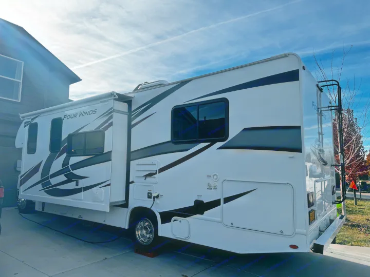 Side view of a white Four Winds RV rental with its slide-out extended, parked on a driveway under a blue sky.. Thor Motor Coach Four Winds 2022