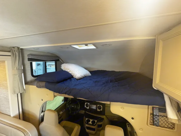 RV rental interior: A comfortable bed is visible above the driver's cab, featuring dark blue bedding and a window.. Thor Motor Coach Four Winds 2022