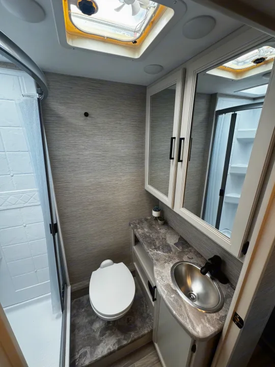 Bright RV rental bathroom with skylight, compact shower, toilet, and vanity with sink and mirrored cabinet.. Thor Motor Coach Four Winds 2022