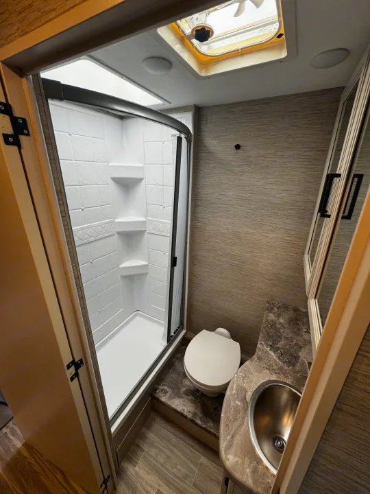 Clean RV rental bathroom featuring a stand-up shower, toilet, sink, and natural light from a skylight.. Thor Motor Coach Four Winds 2022
