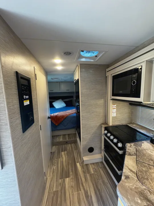 RV rental interior featuring a compact kitchen with a microwave and stove, main control panel, and a cozy bedroom.. Thor Motor Coach Four Winds 2022