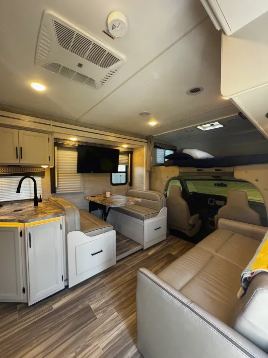 Modern RV rental interior with kitchen, dining booth, sofa, and overhead bunk. Ideal for family travel adventures.. Thor Motor Coach Four Winds 2022