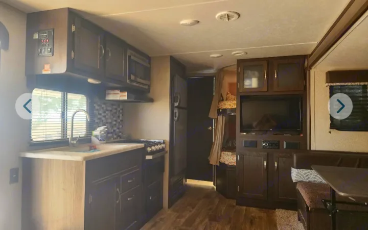 An rv rental interior featuring a modern kitchen, dining area with booth seating, TV, and cozy bunk beds.. Keystone RV Springdale 2019