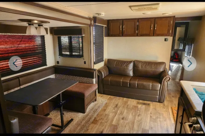 Spacious RV rental living area featuring a dinette, brown sofa, and kitchen counter. Ideal for comfortable travel.. Keystone RV Springdale 2019