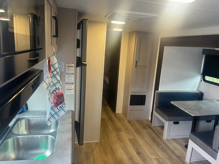 Bright RV rental interior: well-equipped kitchen with dual sinks, microwave, fridge, and cozy dinette seating area.. Heartland RVs Prowler Lynx 302 BHX 2025