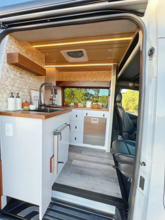 Explore this modern rv rental interior with a built-in kitchen, sleek wood accents, and window views for your next adventure.. Mercedes Sprinter Van 170 4x4 2022
