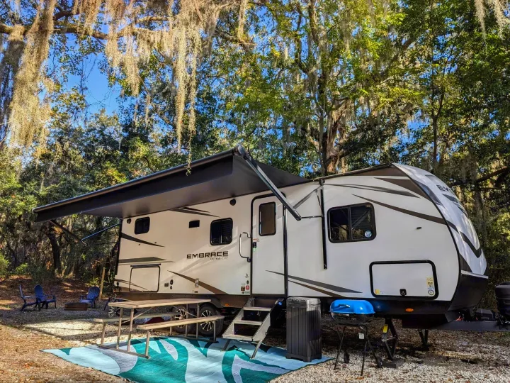 Perfect rv rental setup: modern travel trailer at a shaded campsite with an awning, picnic table & grill.. Cruiser Rv Corp Other 2024