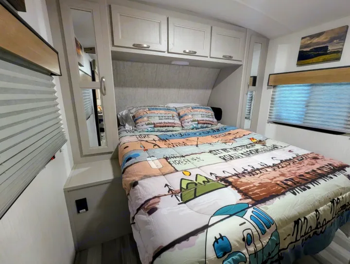 Inside an RV rental: a bright bedroom with a patterned comforter, overhead storage, and window blinds for comfort.. Cruiser Rv Corp Other 2024